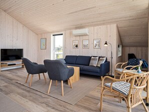 A modern living room with a sofa, chairs, a TV, and a dining area.