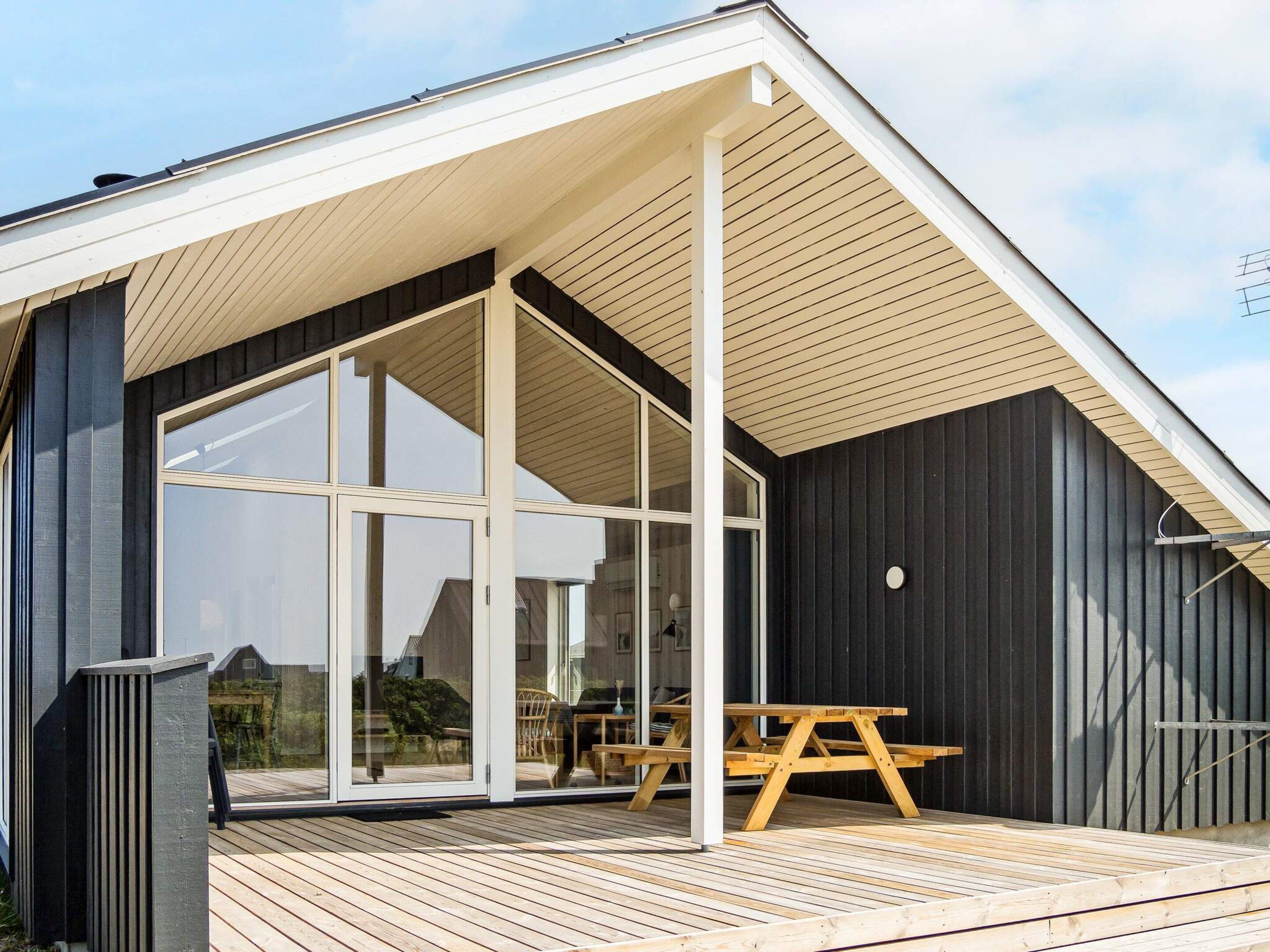 A modern building with a sloped roof, large glass windows, and a wooden deck.