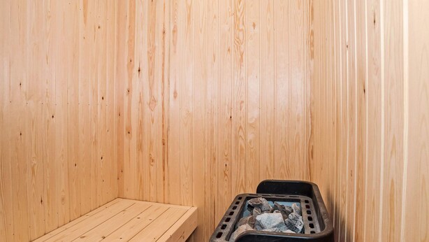 A sauna room with wooden walls, a bench, and a sauna heater. - 8 Person Holiday Home in Harboore (Harboore)
