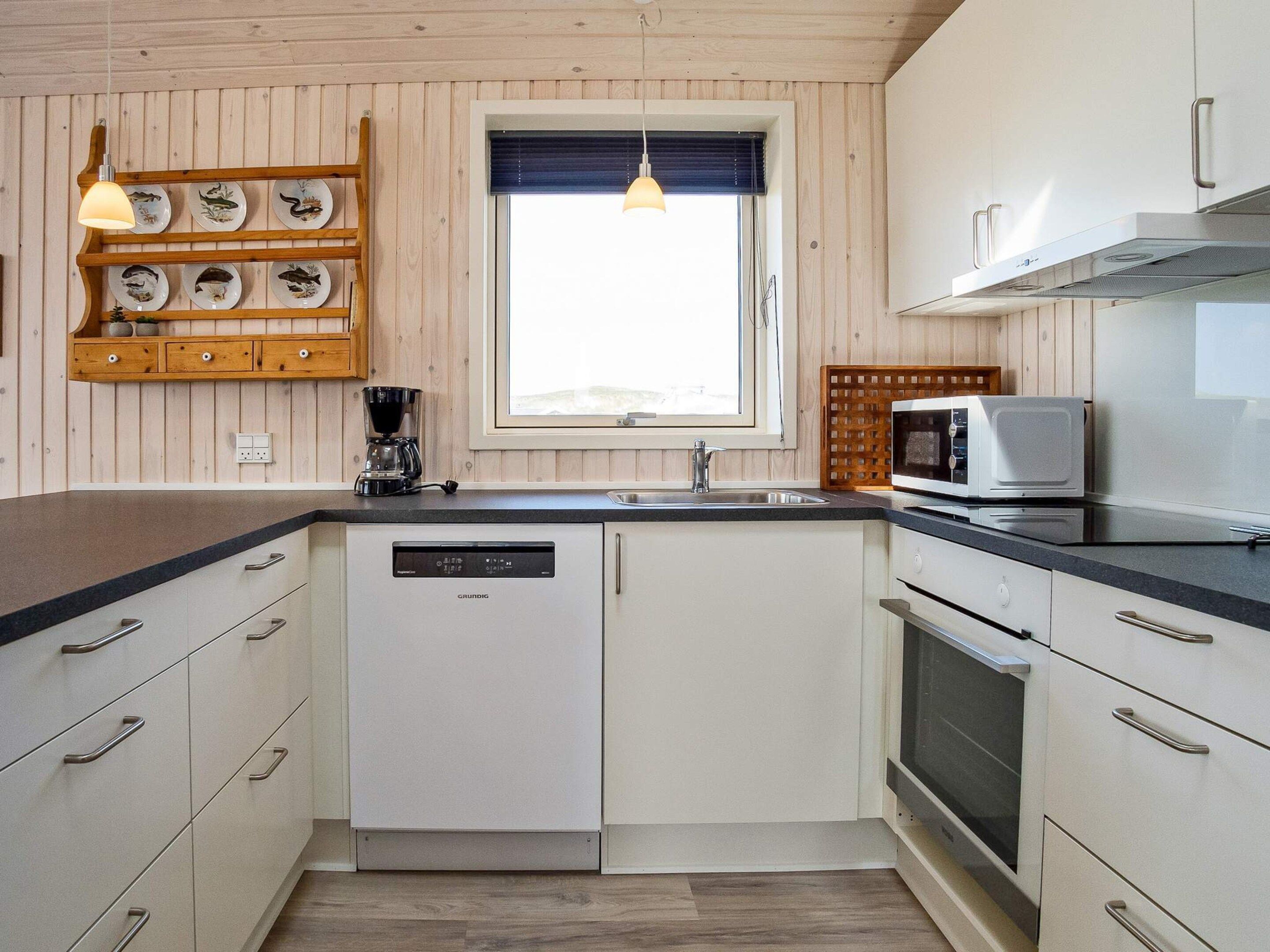 A compact kitchen with white cabinetry, a built-in dishwasher, a microwave, and a coffee maker.