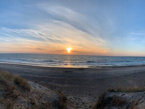 Une plage avec des dunes de sable et un coucher de soleil sur l’océan.