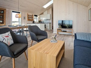 Un espace de vie moderne doté d’un plancher en bois, d’un coin repas avec des chaises, d’un canapé, d’une table basse et d’un téléviseur.