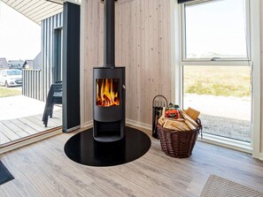 A modern interior with a wood-burning stove, a wicker basket with firewood, and a view through a large window. - 8 Person Holiday Home in Harboore (Harboore)