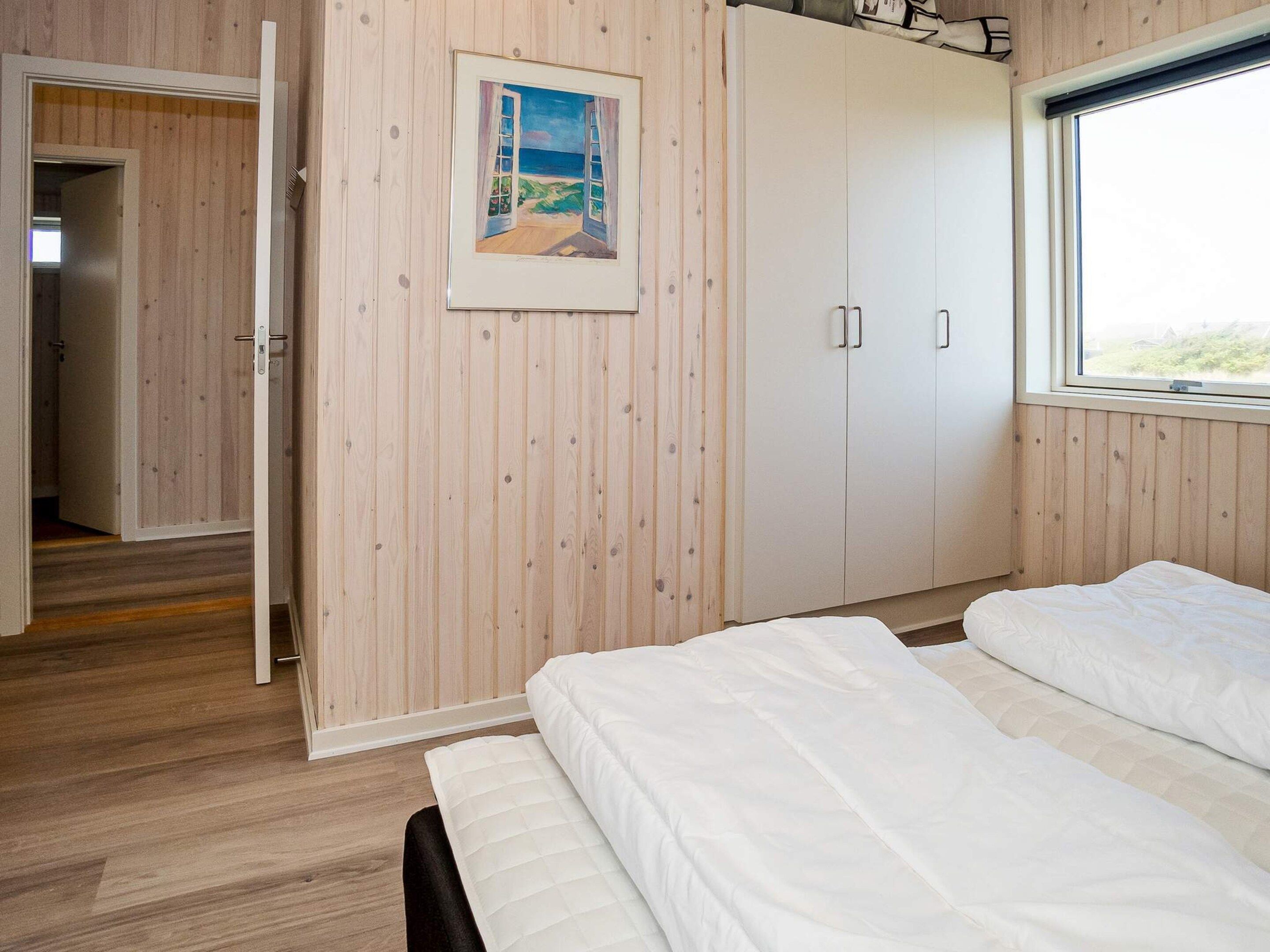 Una camera da letto con pannelli in legno, un letto con biancheria bianca, un armadio e una finestra con vista.