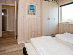 A bedroom with wooden paneling, a bed with white bedding, a wardrobe, and a window with a view. - 8 Person Holiday Home in Harboore (Harboore)
