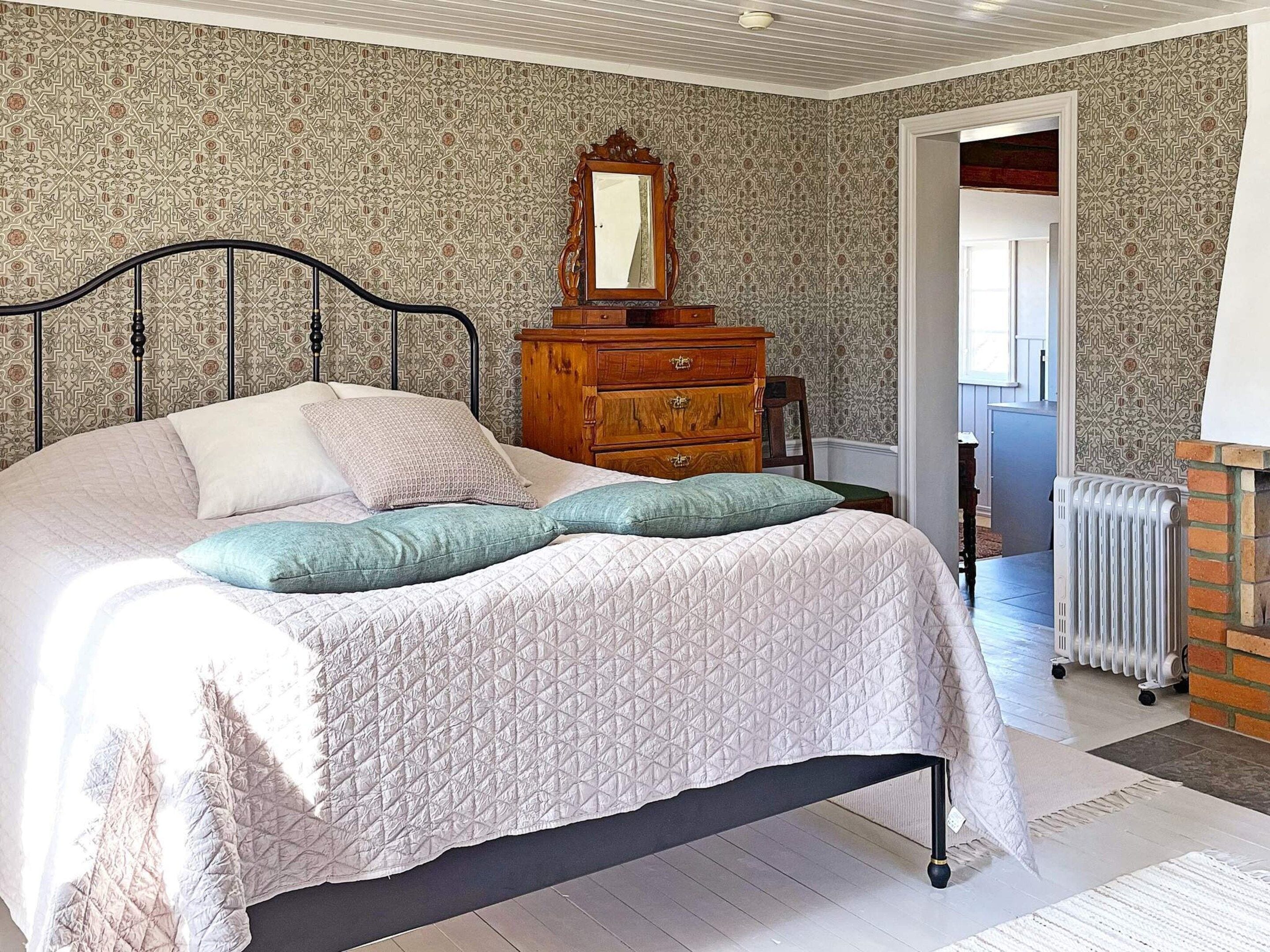 Un dormitorio con cama, cómoda, espejo y radiador.