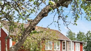 Une maison en bois rouge, avec un toit en pente, entourée de verdure et sous un ciel dégagé.
