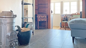 A room with a large metal stove, a wooden cabinet, a wicker chair, and a blue sofa. - 4 Star Holiday Home in Mariestad (Mariestad)