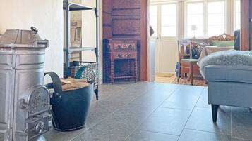 Una habitación con un estufa metálica grande, un armario de madera, una silla de mimbre y un sofá azul.