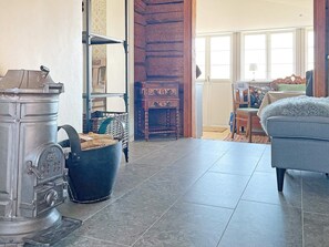 A room with a large metal stove, a wooden cabinet, a wicker chair, and a blue sofa. - 4 Star Holiday Home in Mariestad (Mariestad)