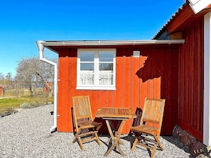 A red wooden building with a window and two wooden chairs and a table outside.