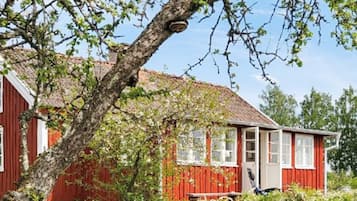 A red wooden house with a sloped roof, surrounded by greenery and a clear sky.
