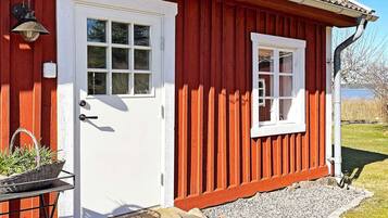 Une maison en bois rouge avec une porte et une fenêtre blanches, un petit porche avec un panier, et une vue dégagée sur le paysage environnant.