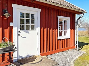 A red wooden house with a white door and window, a small porch with a basket, and a clear view of the surrounding landscape. - 4 Star Holiday Home in Mariestad (Mariestad)