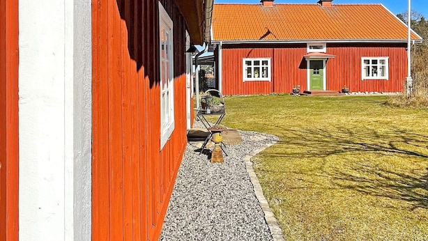 A red building with a sloped roof and a green door, a gravel path leading to the entrance, and a clear blue sky. - 4 Star Holiday Home in Mariestad (Mariestad)