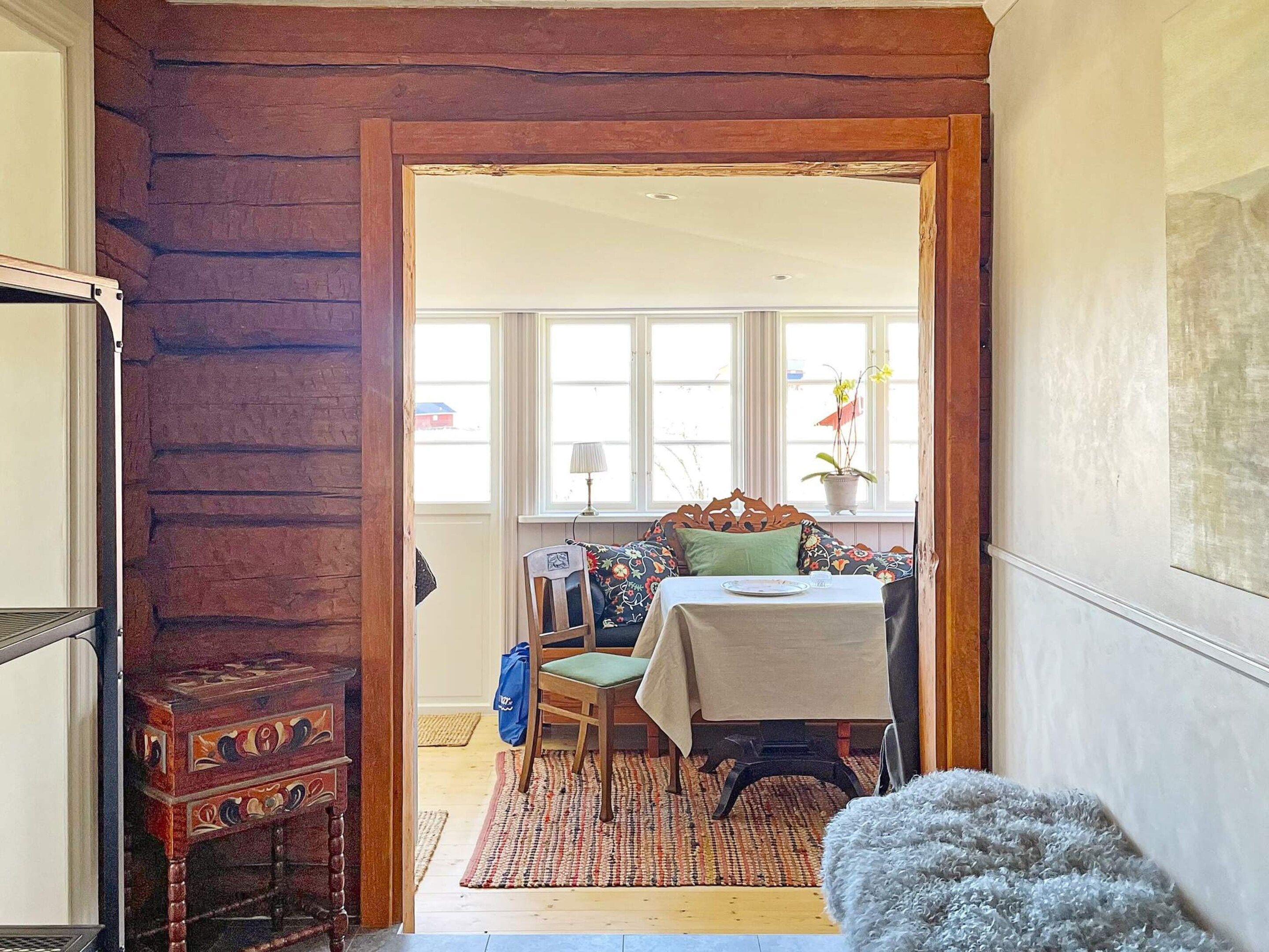 A room with a wooden door, a dining table with chairs, a window with curtains, and a small rug.