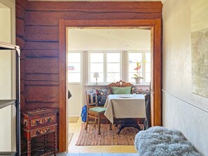 A room with a wooden door, a dining table with chairs, a window with curtains, and a small rug. - 4 Star Holiday Home in Mariestad (Mariestad)