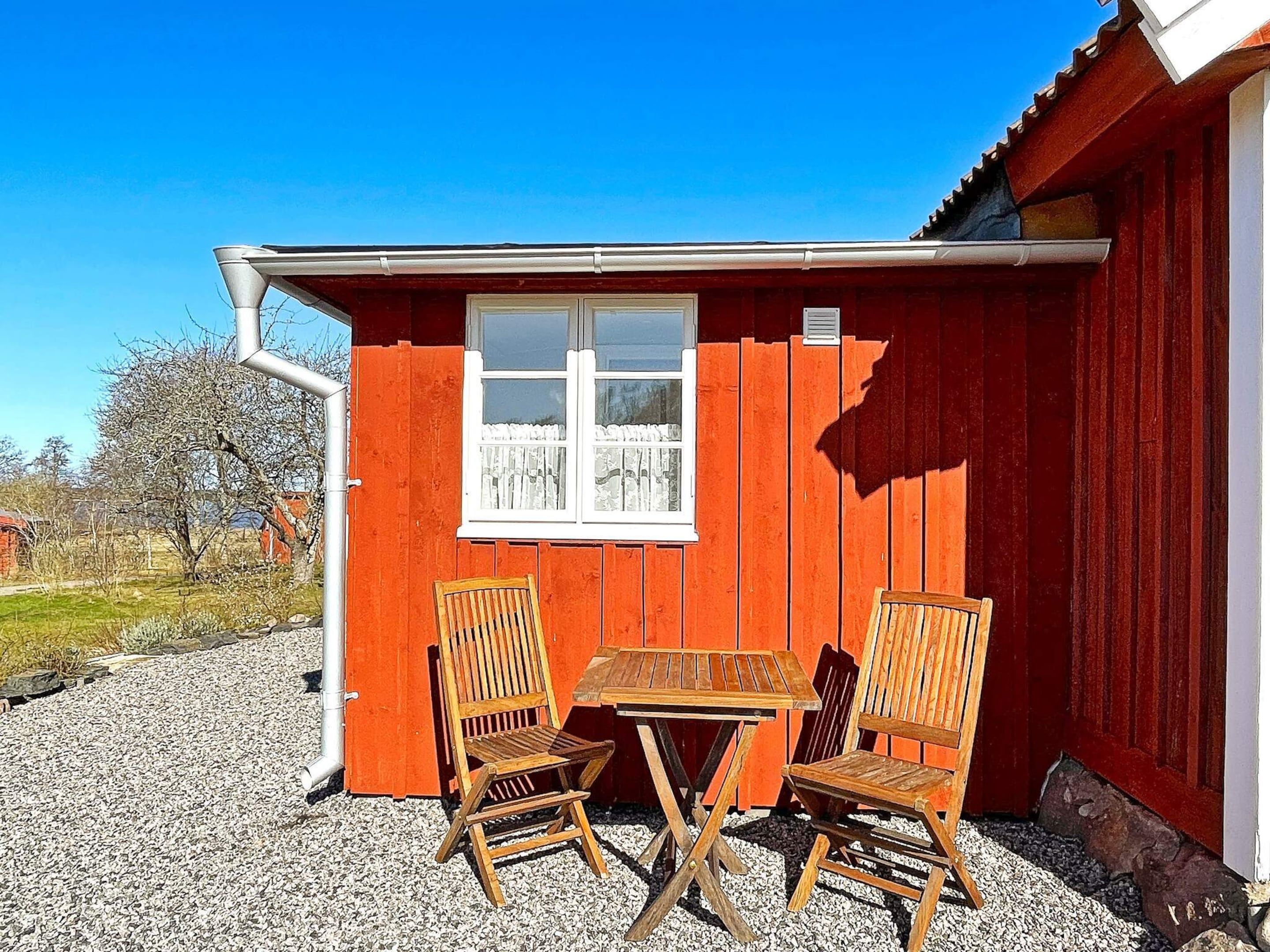 Un bâtiment en bois rouge, avec une fenêtre, et deux chaises et une table en bois à l’extérieur.