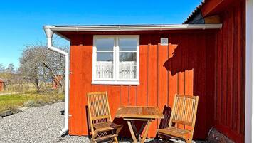Un bâtiment en bois rouge, avec une fenêtre, et deux chaises et une table en bois à l’extérieur.