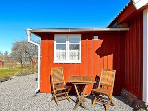 A red wooden building with a window and two wooden chairs and a table outside. - 4 Star Holiday Home in Mariestad (Mariestad)