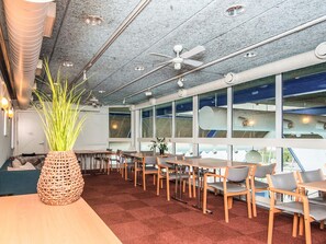 A modern interior with a long table and chairs, large windows, and a ceiling fan. - 4 Person Holiday Home in Hejls (Hejls)