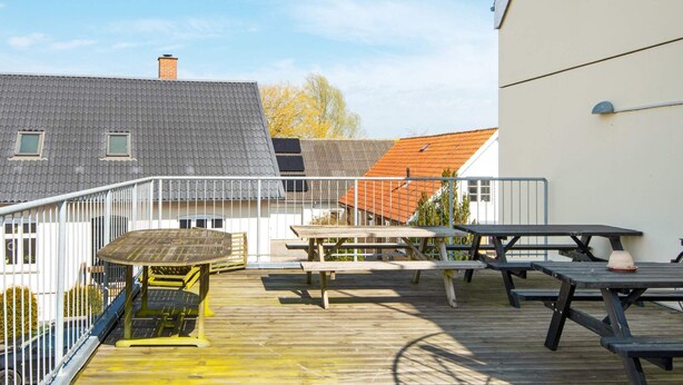 Une terrasse en bois avec des tables de pique-nique et une rambarde en métal.