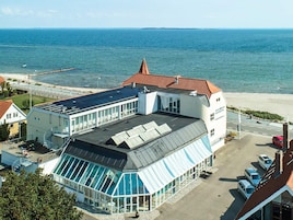 Un hotel costero con un amplio invernadero de vidrio, piscina y vistas al mar.