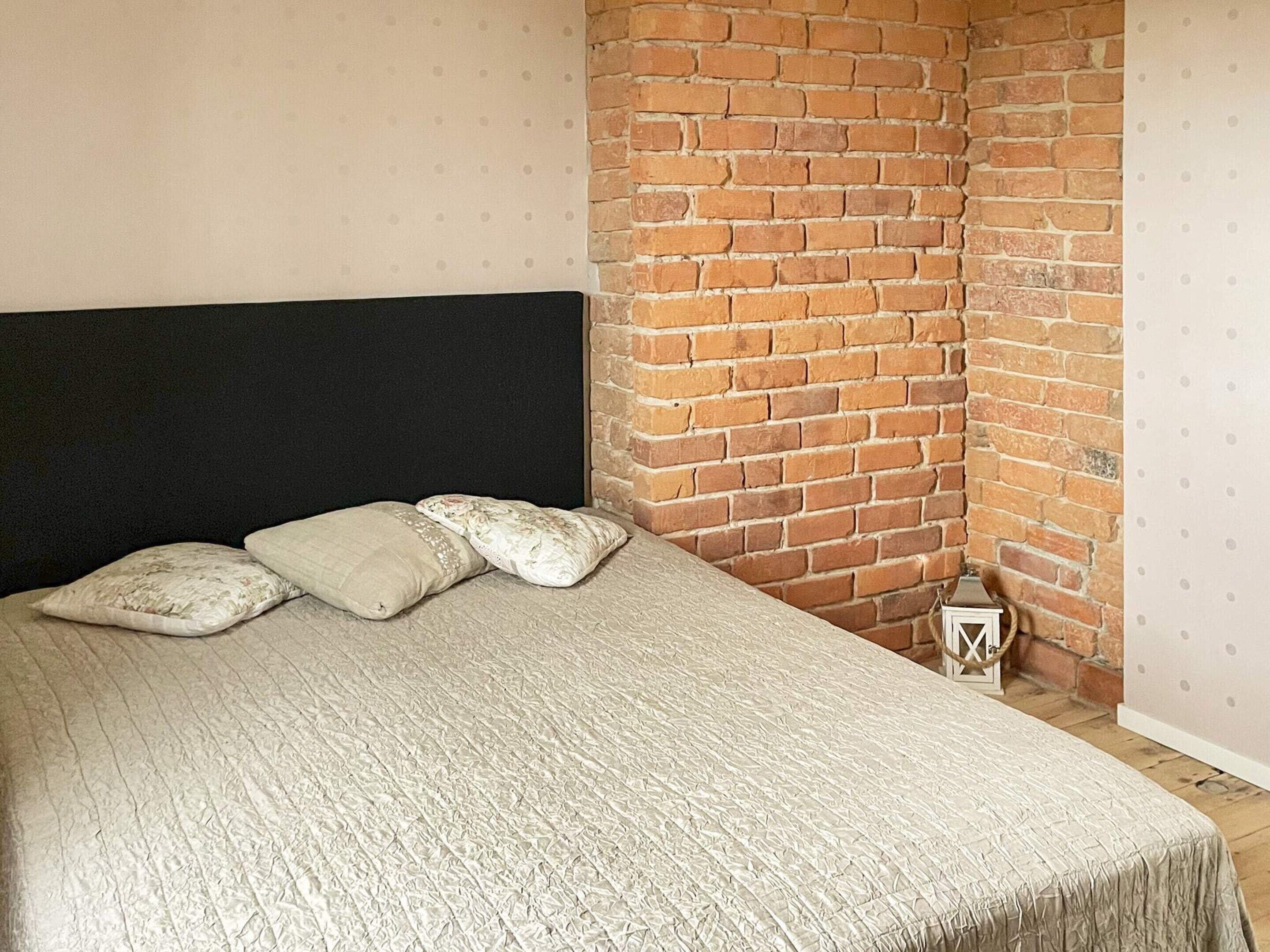 Una cama con cabecera negra, colcha color beige y tres almohadas.