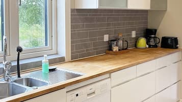 A modern kitchen with a dishwasher, a coffee maker, and a kettle on the counter.