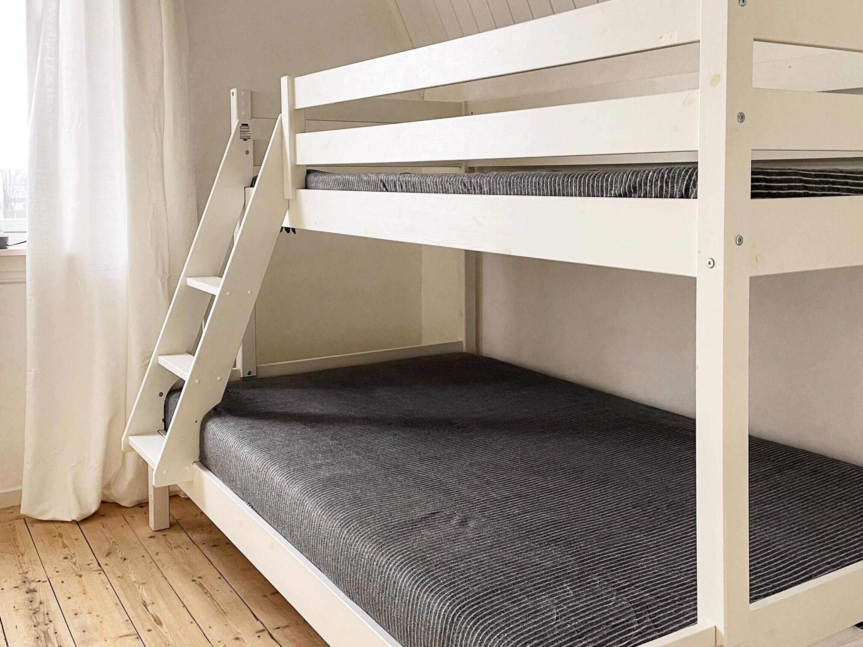 Una cama individual superpuesta con escalera, un colchón gris y suelo de madera.