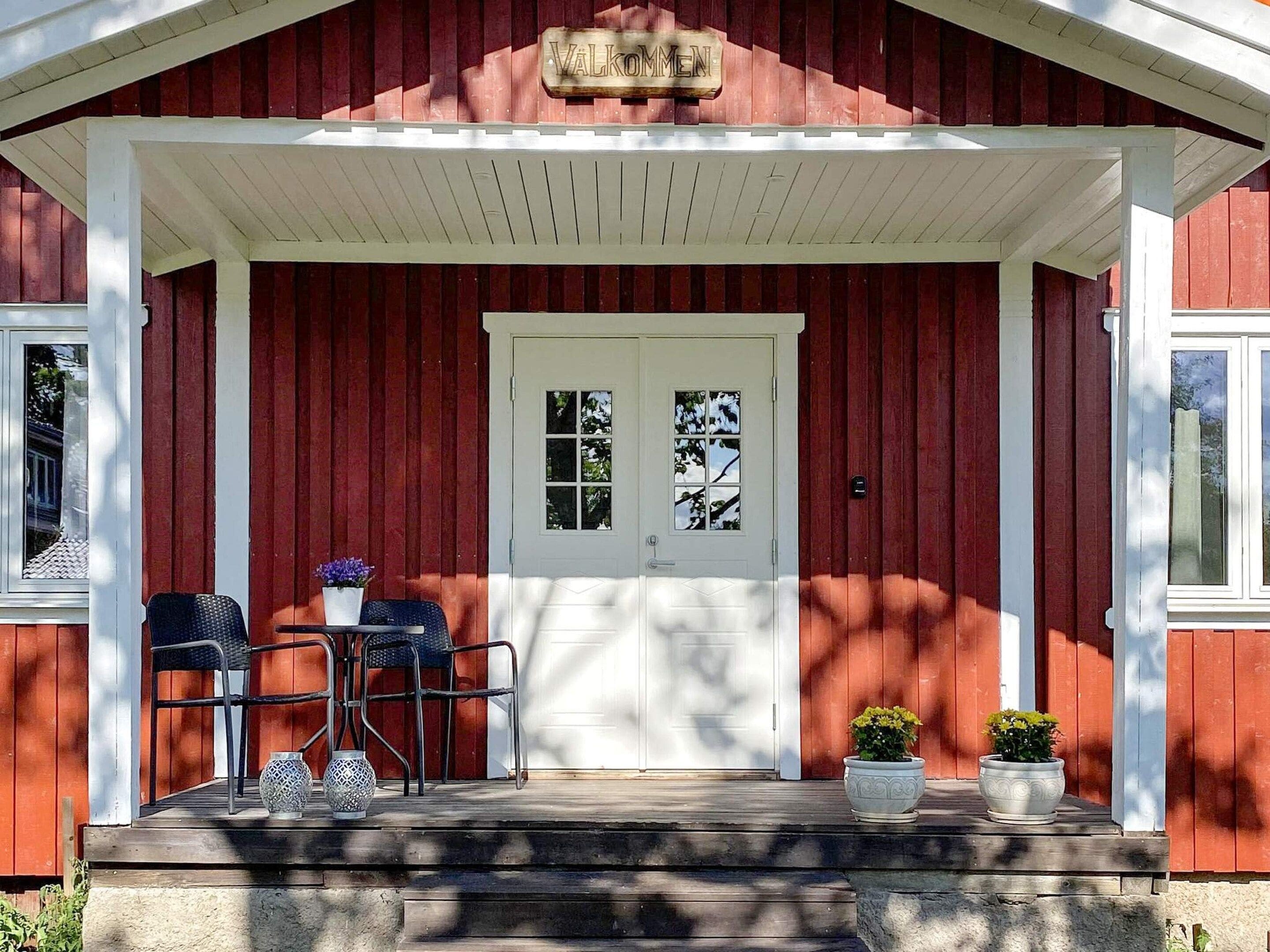 A red wooden building with a white porch, a double door, and two potted plants.