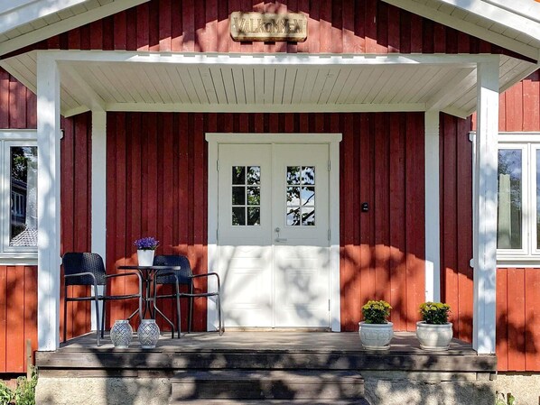 A red wooden building with a white porch, a double door, and two potted plants. - 4 Star Holiday Home in Vastra Amtervik (Vastra Amtervik)
