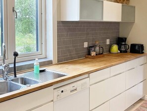 Une cuisine équipée d’un lave-vaisselle, d’une machine à café et d’une bouilloire posée sur le plan de travail.