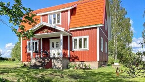 Ein zweistöckiges Haus mit roter Fassade und einem Ziegeldach, mit einer Veranda, Treppen und Blumentöpfen.