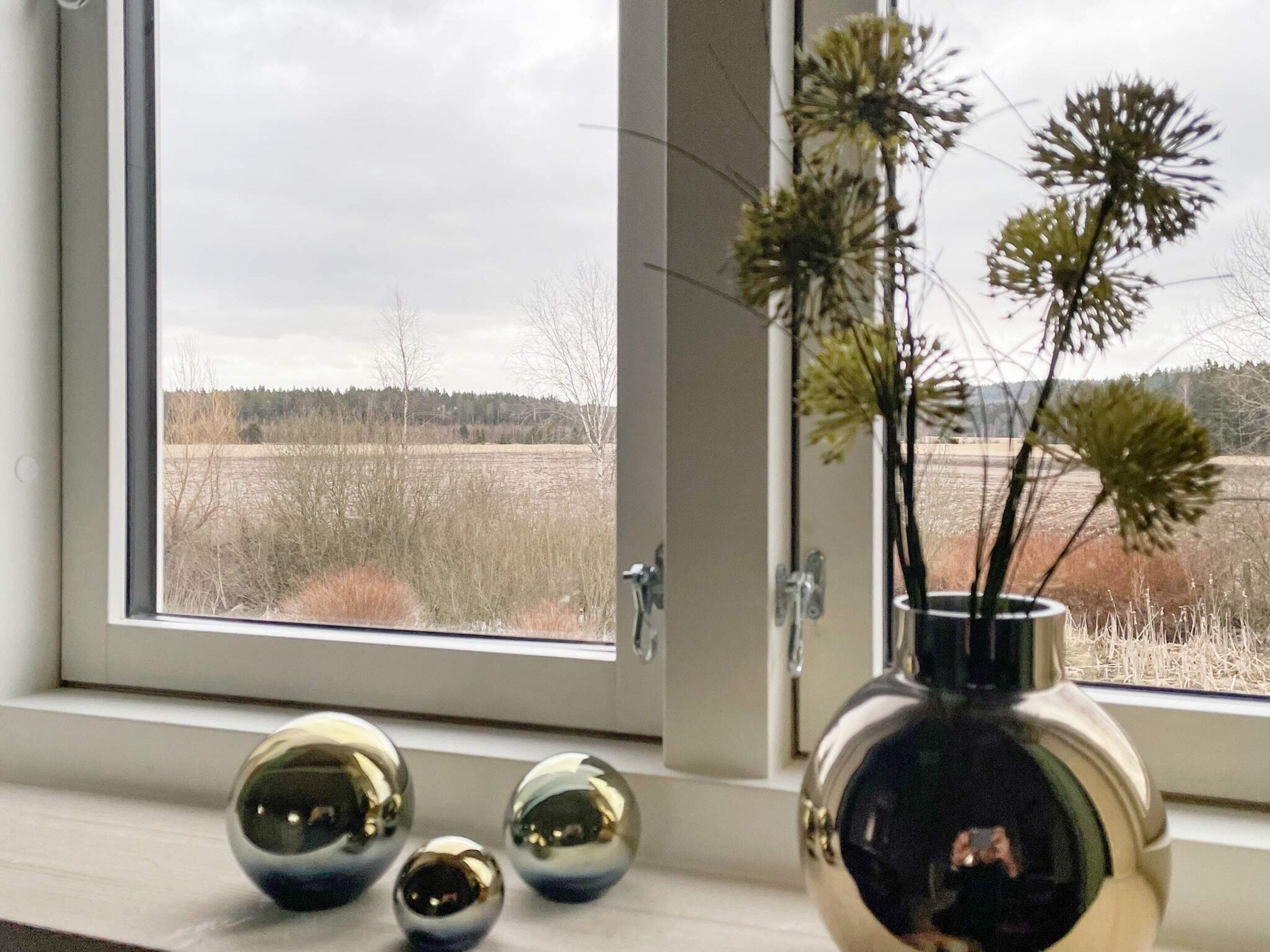 Una ventana con vista a un campo y un florero con plantas secas en el alféizar.