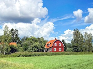 A red barn with a sloped roof, surrounded by a green field and trees. - 4 Star Holiday Home in Vastra Amtervik (Vastra Amtervik)