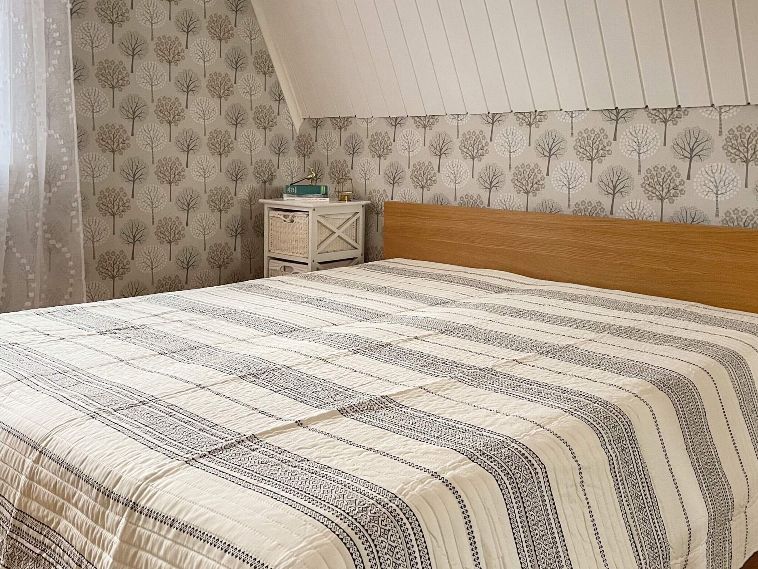 Un dormitorio con una cama, una mesita de noche y una pared decorada con un estampado de árbol.