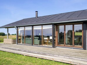 A modern building with large glass windows, a wooden deck, and a chimney. - 8 Person Holiday Home in Store Fuglede (Store Fuglede)