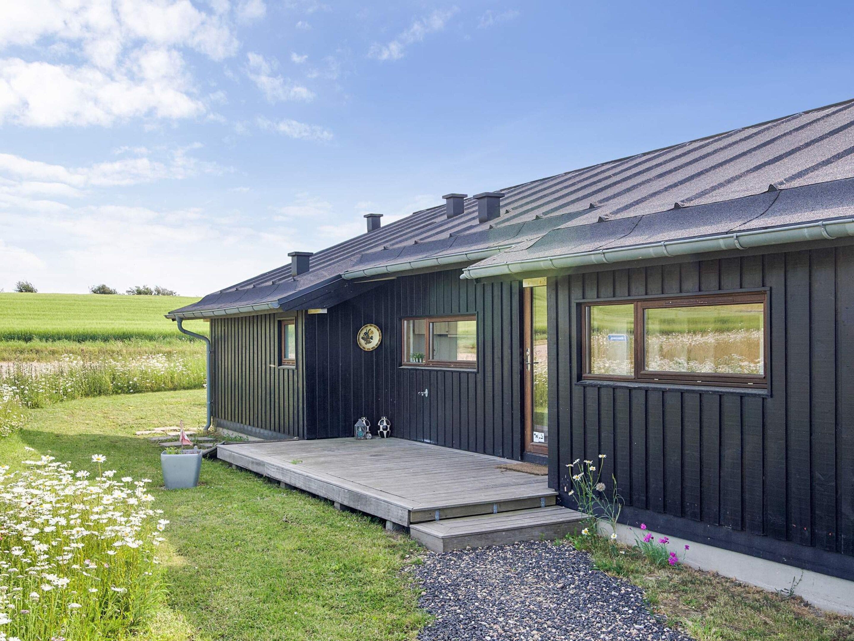 A dark wooden house with a porch, a small garden with flowers, and a clear sky.