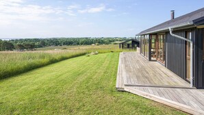 Una casa moderna con terraza de madera, ventanas amplias y vista al campo.