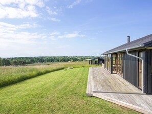 A modern house with a wooden deck, large windows, and a view of the countryside.