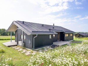 A modern house with a sloped roof, a covered porch, and a garden with white flowers. - 8 Person Holiday Home in Store Fuglede (Store Fuglede)