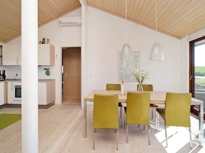 A modern kitchen with built-in appliances, a dining area with a wooden table and green chairs, and a large window providing a view of the outdoors. - 8 Person Holiday Home in Store Fuglede (Store Fuglede)