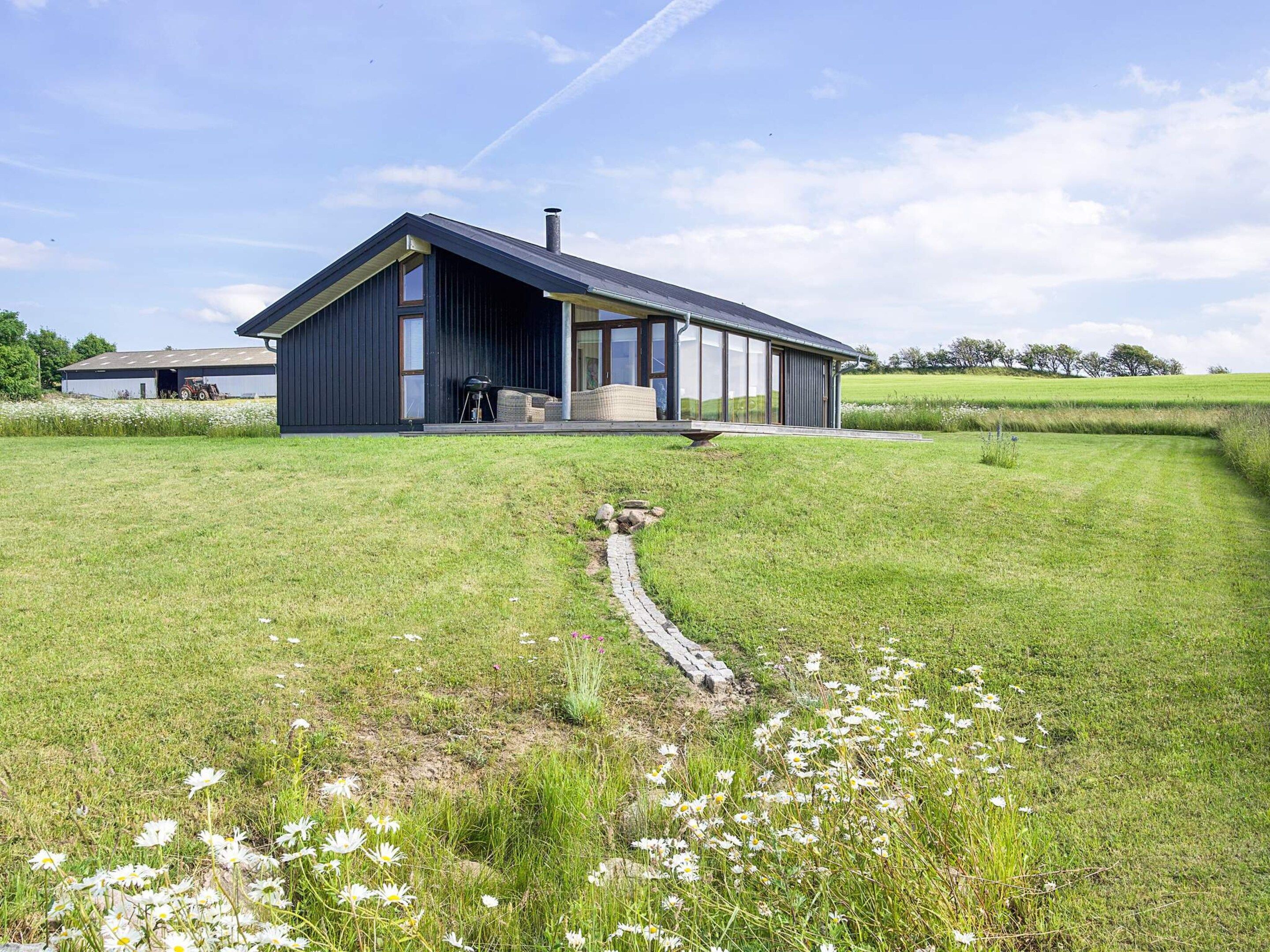 A modern house with a large deck, surrounded by a grassy field and a small stream.