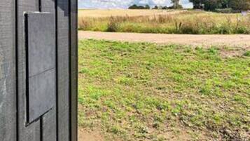 A view through a door into a field with a dirt path and distant trees.