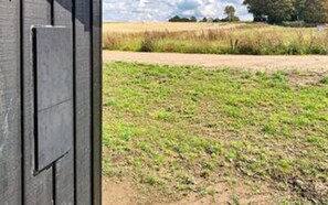 A view through a door into a field with a dirt path and distant trees.