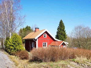Une maison rouge avec un toit en pente, entourée d’arbres et d’arbustes.