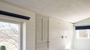A room with a bed, a window with a view of bare trees, and a door with a light switch on the wall.