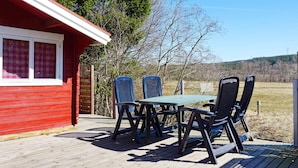 A red cabin with a deck, outdoor seating, and a view of trees and hills. - 4 Person Holiday Home in Hedekas (Hedekas)
