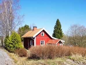 A red house with a sloped roof, surrounded by trees and shrubs.